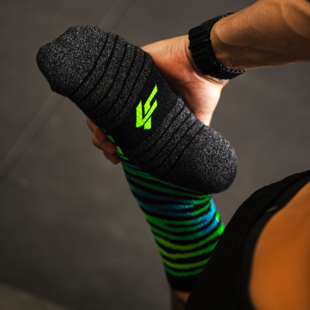 Person holding a Lightfeet Predator black aqua yellow sock against a dark background