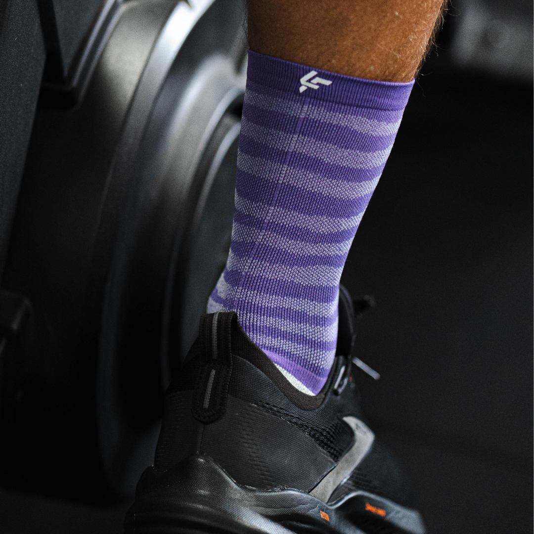 Person wearing Lightfeet Raster purple half crew striped socks with a black shoe on a blurred background