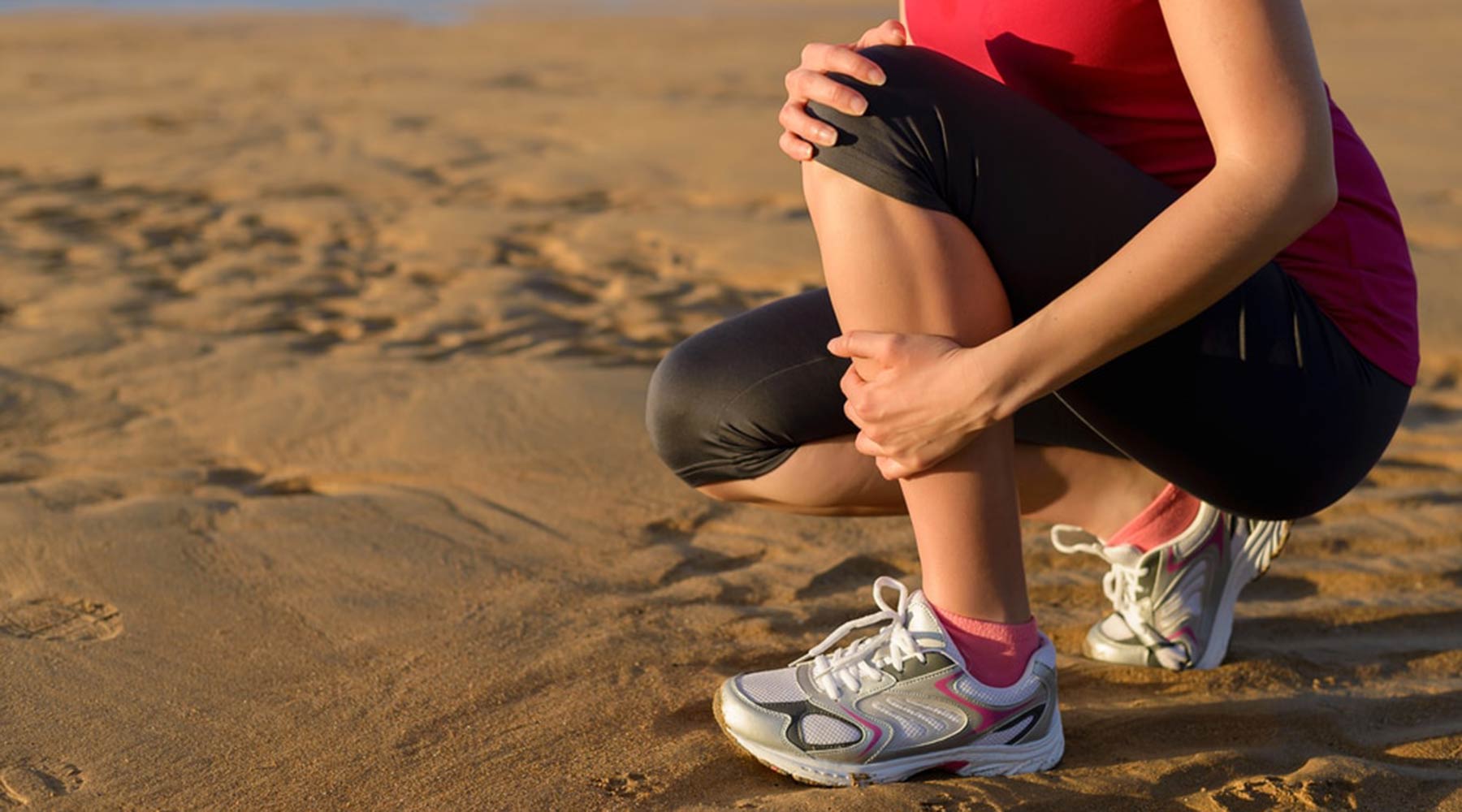 Woman on beach in exercise clothing, clutching shin