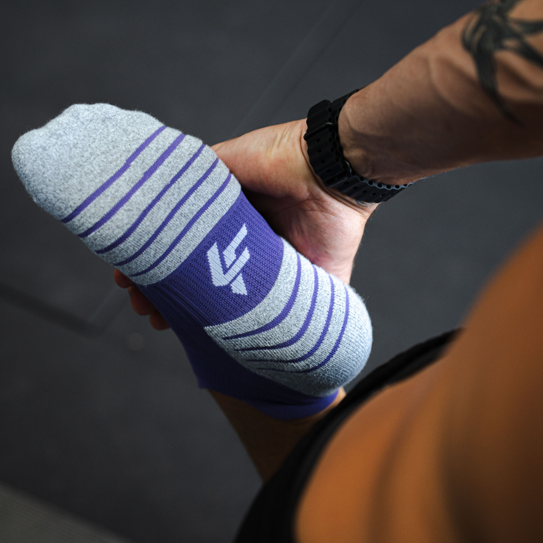 Hand holding aLightfeet Performance Purple Ankle sock with a Lightfeet logo against a dark background