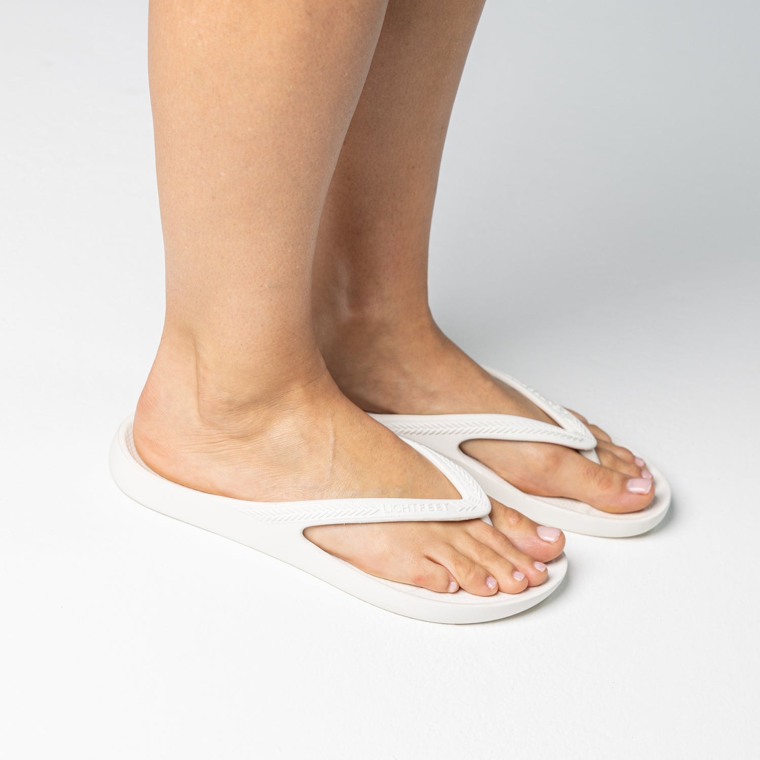 Person walking on and off screen wearing White Lightfeet Arch Support Thongs